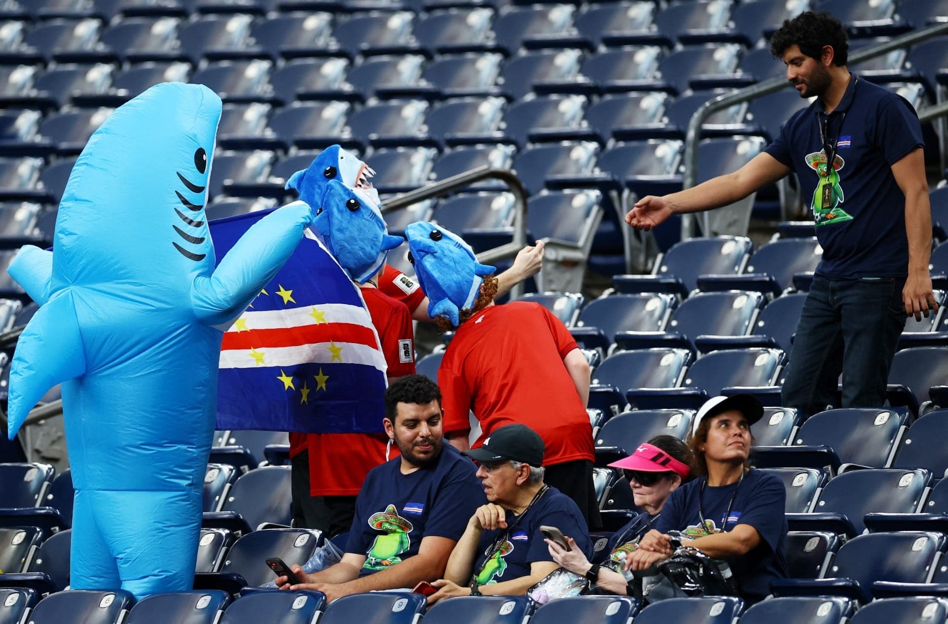 Torcedores de Cabo Verde vestidos de tubarões posam para uma foto dentro do estádio antes da partida.