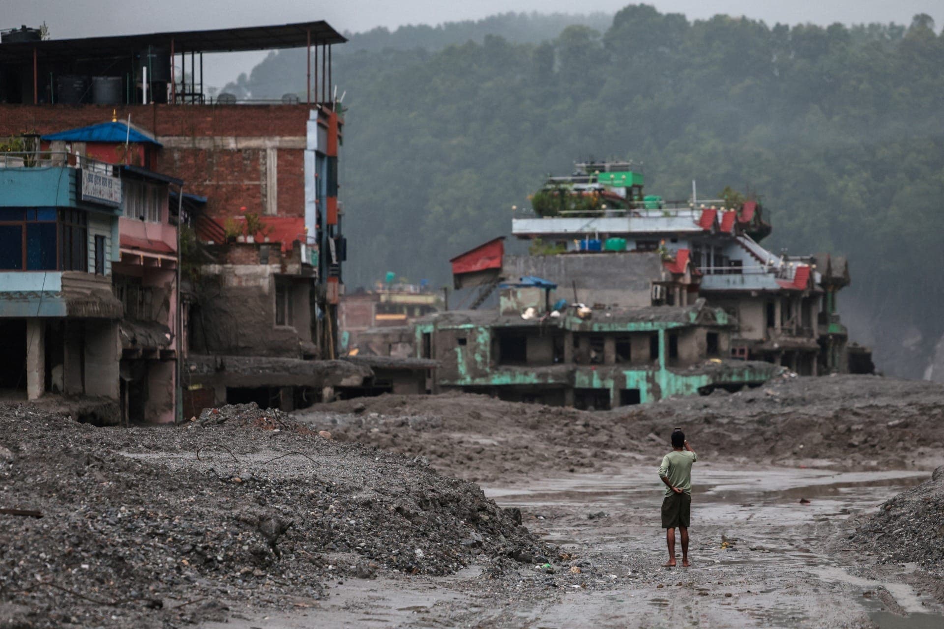 Homem fotografa prédios danificados após enchentes e deslizamento de terra em Trishuli, no distrito de Nuwakot, no Nepal